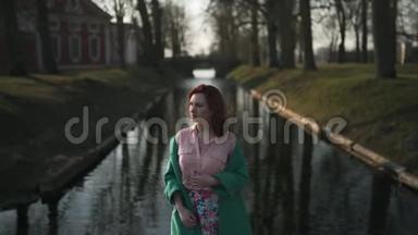在温<strong>暖</strong>的春天天气里，穿着绿色时尚夹克的年轻女子在皇<strong>宫</strong>运河附近放松-红头发